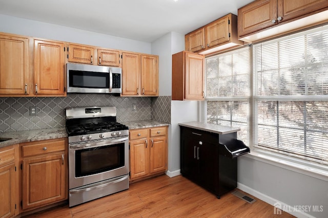 kitchen with decorative backsplash, stainless steel appliances, light stone countertops, and light hardwood / wood-style flooring