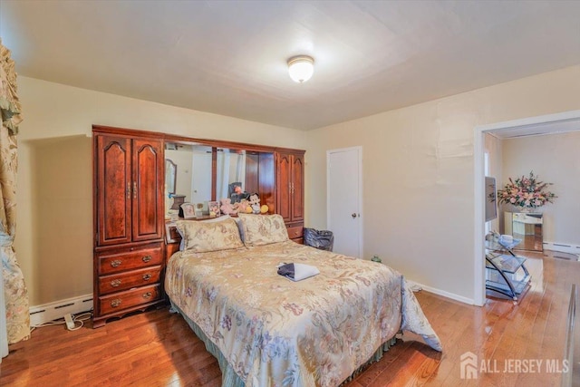 bedroom featuring baseboard heating, a baseboard radiator, light wood-style flooring, and baseboards