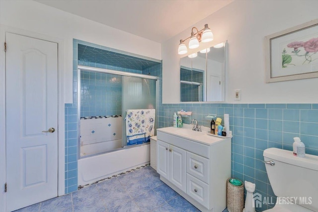 bathroom with tile walls, toilet, wainscoting, combined bath / shower with glass door, and vanity