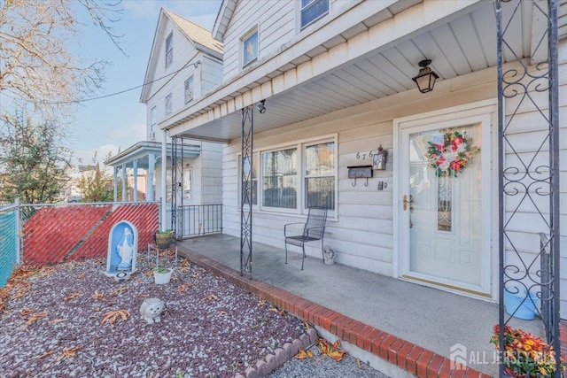 view of exterior entry featuring a porch and fence