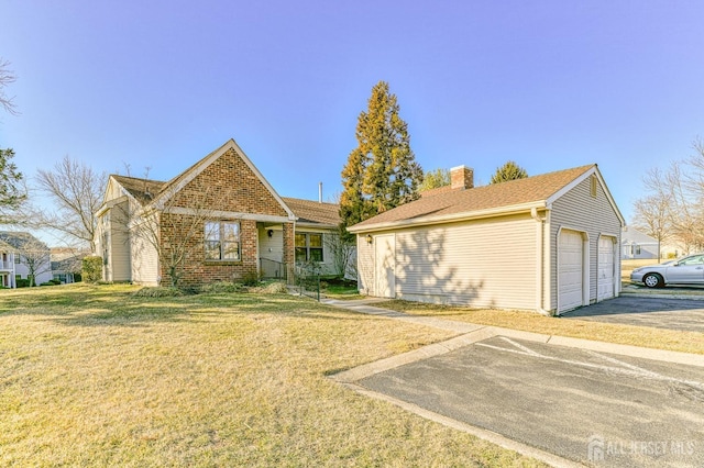 view of front of property with a detached garage, an outdoor structure, a front yard, brick siding, and a chimney