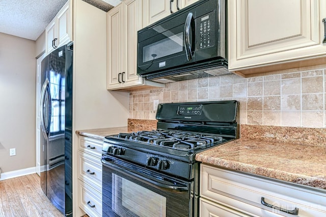 kitchen with baseboards, light wood finished floors, black appliances, cream cabinetry, and backsplash