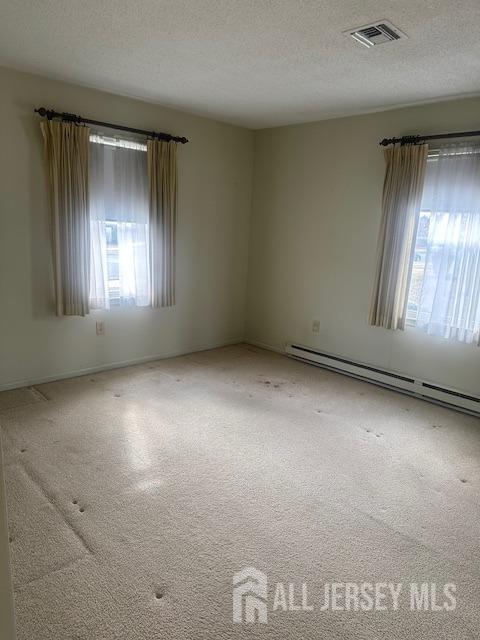 spare room featuring a textured ceiling, carpet, visible vents, and a baseboard radiator