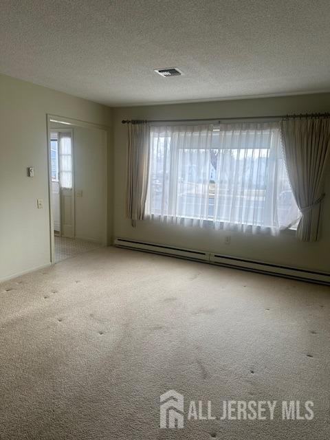 carpeted empty room featuring baseboard heating, a textured ceiling, and visible vents