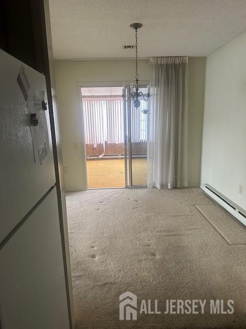 unfurnished dining area featuring visible vents, a chandelier, carpet flooring, baseboard heating, and a textured ceiling