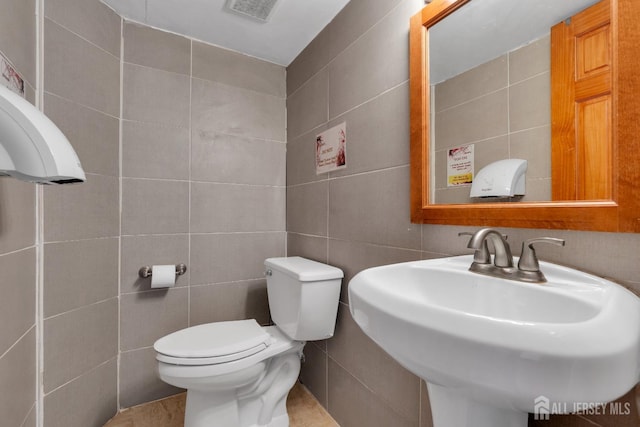 half bath featuring visible vents, toilet, tile walls, and a sink