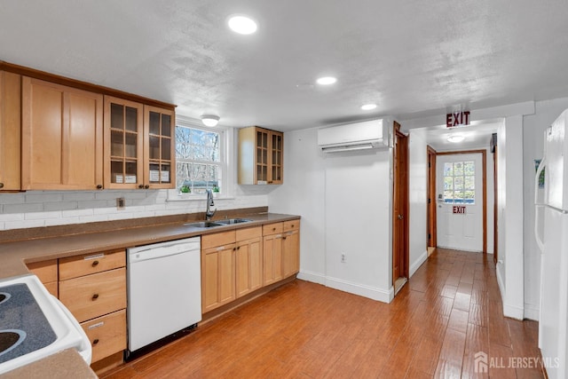 kitchen with a wealth of natural light, light wood-type flooring, an AC wall unit, a sink, and white appliances