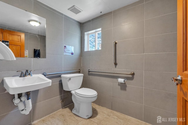 half bathroom featuring visible vents, a sink, tile patterned flooring, tile walls, and toilet