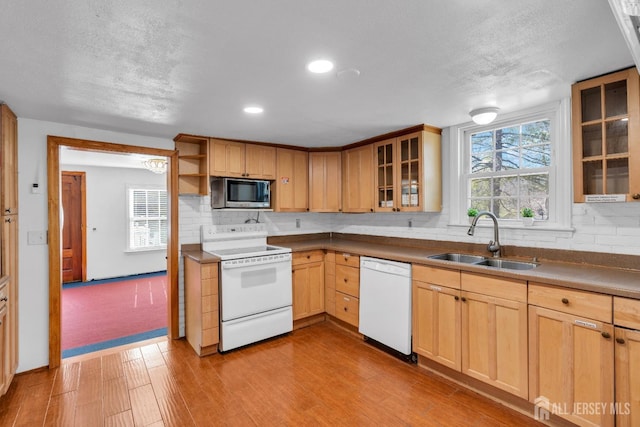 kitchen featuring backsplash, light brown cabinets, wood finished floors, white appliances, and a sink