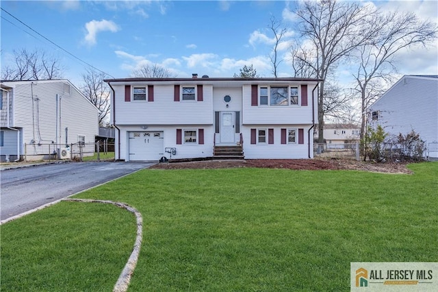 bi-level home featuring entry steps, aphalt driveway, an attached garage, fence, and a front yard