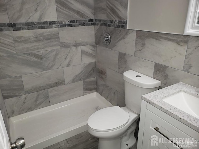 bathroom featuring tiled shower, vanity, toilet, and tile walls