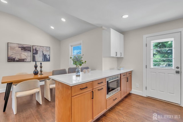 kitchen with stainless steel microwave, light wood finished floors, light countertops, a peninsula, and recessed lighting
