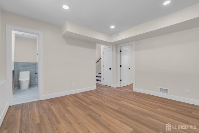 finished below grade area featuring stairway, baseboards, wood finished floors, and recessed lighting