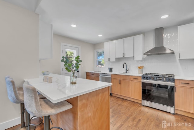 kitchen with gas range, wall chimney exhaust hood, light wood-type flooring, a sink, and a kitchen bar