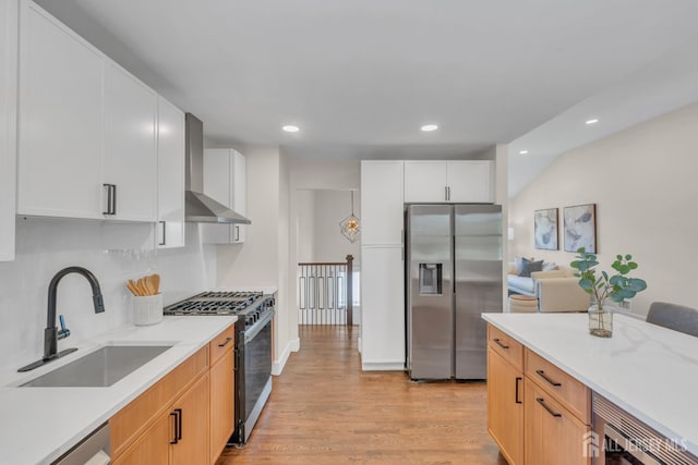 kitchen with stainless steel refrigerator with ice dispenser, range with gas stovetop, a sink, wall chimney exhaust hood, and light wood-type flooring