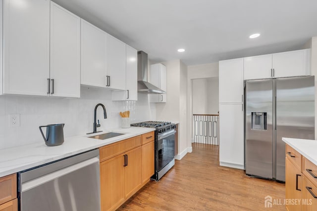 kitchen featuring appliances with stainless steel finishes, wall chimney exhaust hood, a sink, backsplash, and light wood-style floors
