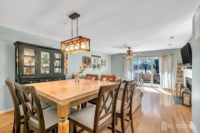 dining room with light wood finished floors, a fireplace, a ceiling fan, and baseboards