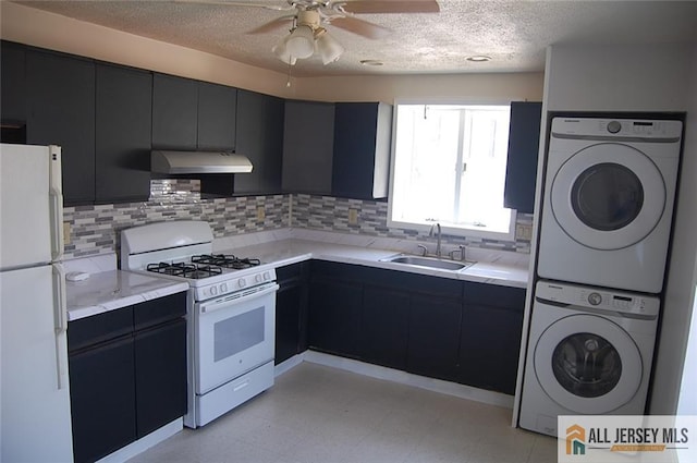 kitchen featuring white appliances, a textured ceiling, under cabinet range hood, a sink, and stacked washer / drying machine