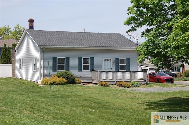 new england style home with a chimney, roof with shingles, a front yard, and a deck
