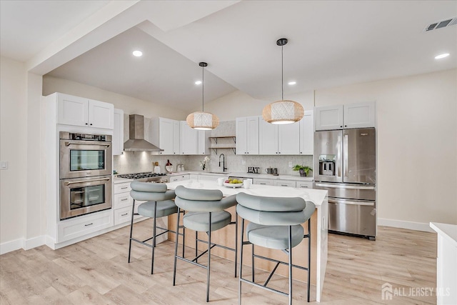 kitchen with appliances with stainless steel finishes, white cabinetry, wall chimney range hood, sink, and hanging light fixtures