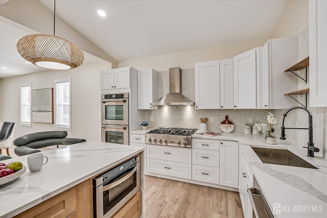 kitchen featuring white cabinetry, stainless steel appliances, wall chimney range hood, pendant lighting, and light stone counters