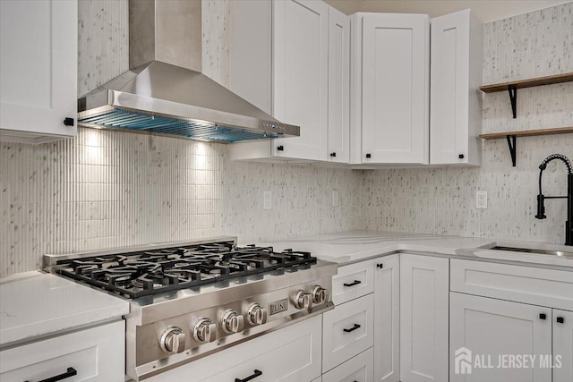 kitchen with stainless steel gas stovetop, light stone countertops, wall chimney exhaust hood, white cabinets, and sink