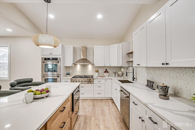 kitchen with appliances with stainless steel finishes, decorative light fixtures, white cabinetry, wall chimney range hood, and sink