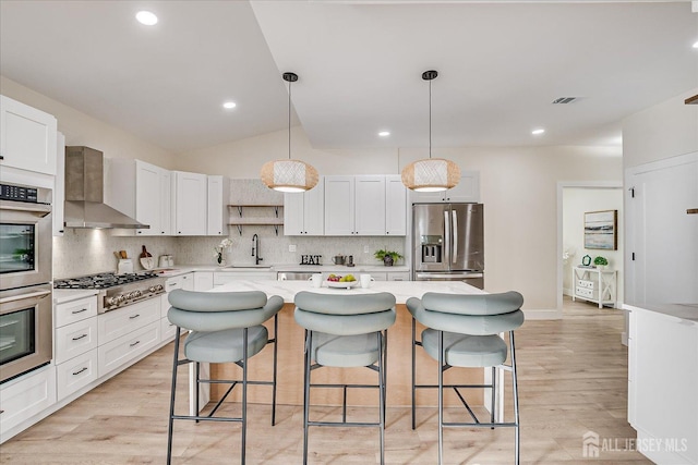 kitchen featuring white cabinets, appliances with stainless steel finishes, a center island, wall chimney exhaust hood, and sink