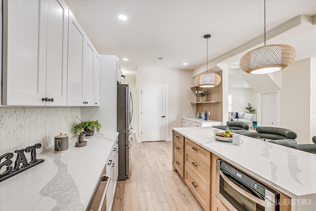 kitchen featuring tasteful backsplash, white cabinetry, hanging light fixtures, light stone countertops, and stainless steel fridge