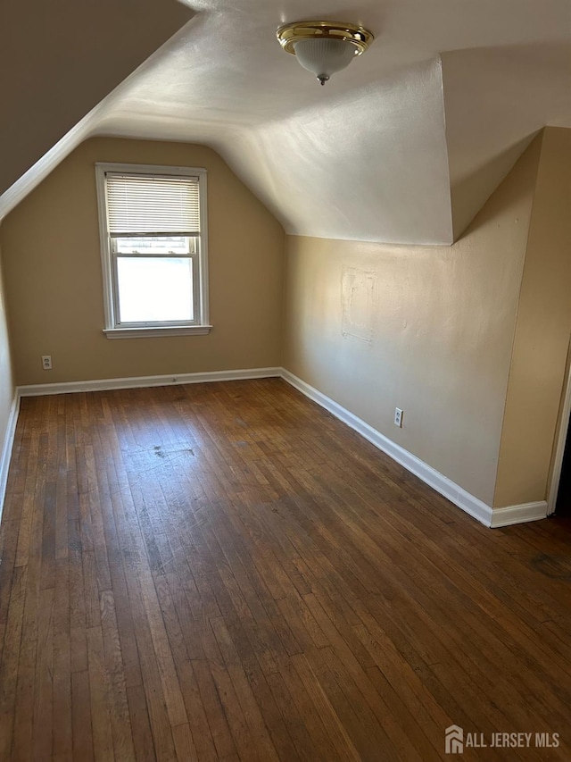 additional living space featuring baseboards, dark wood finished floors, and vaulted ceiling