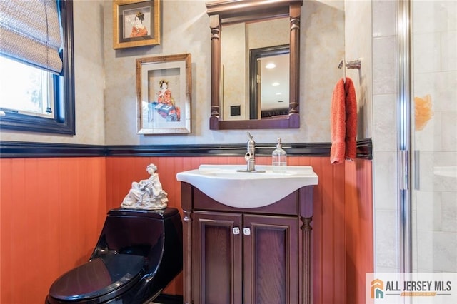 bathroom featuring vanity, a tile shower, and a wainscoted wall