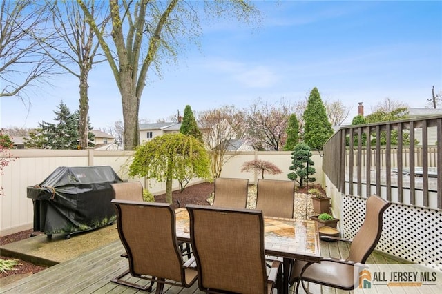deck with outdoor dining area, a fenced backyard, and a grill