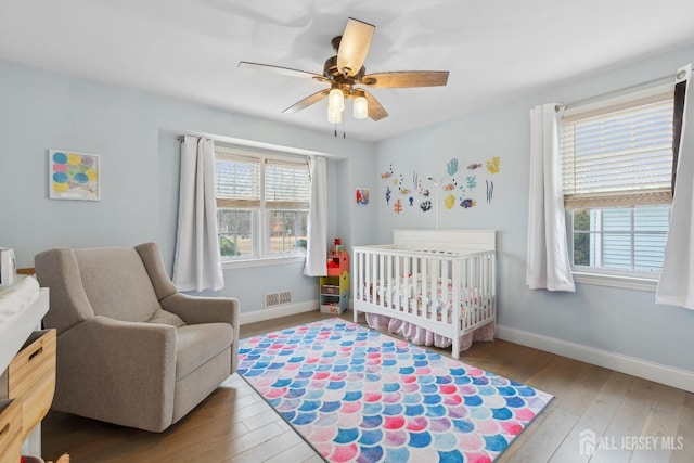 bedroom featuring baseboards, visible vents, light wood finished floors, and a crib