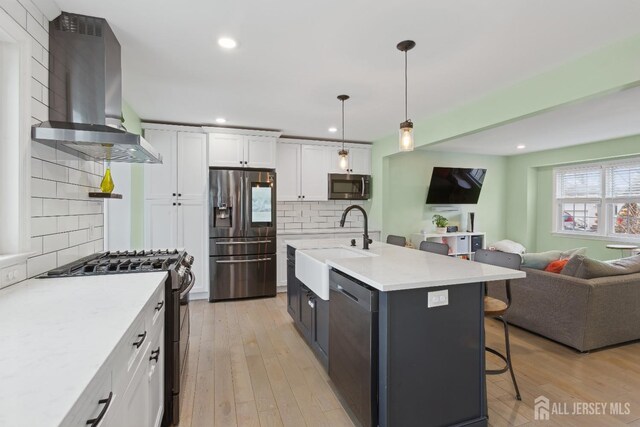 kitchen with decorative light fixtures, white cabinetry, backsplash, stainless steel appliances, and wall chimney range hood