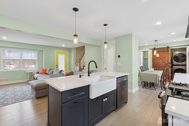 kitchen featuring a barn door, stacked washer / dryer, appliances with stainless steel finishes, decorative light fixtures, and light countertops