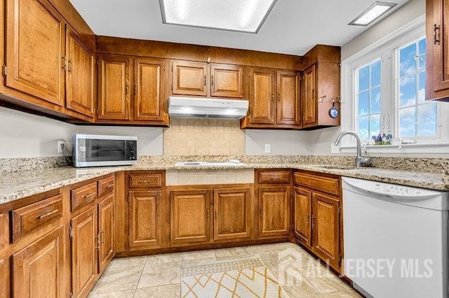 kitchen featuring under cabinet range hood, stainless steel microwave, a sink, brown cabinetry, and dishwasher