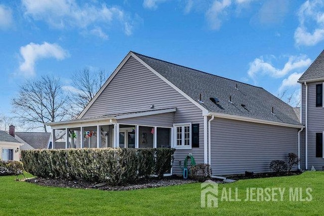 back of house with a lawn, a sunroom, and roof with shingles