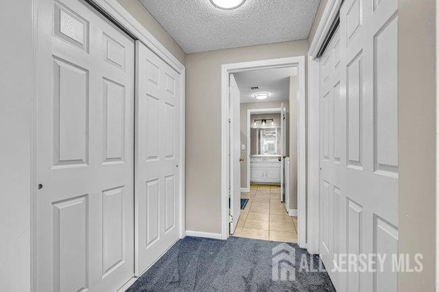 hallway with baseboards, a textured ceiling, carpet, and tile patterned flooring