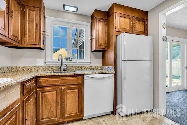 kitchen featuring white appliances, light stone countertops, brown cabinets, and a sink