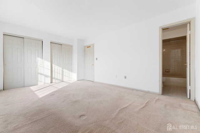 unfurnished bedroom featuring light carpet, two closets, and ensuite bath