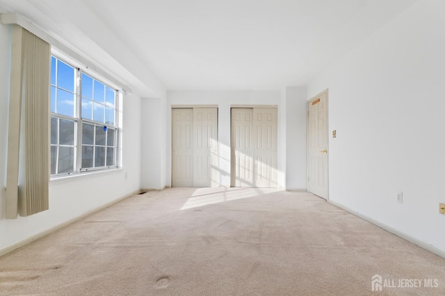 unfurnished bedroom featuring light colored carpet and two closets