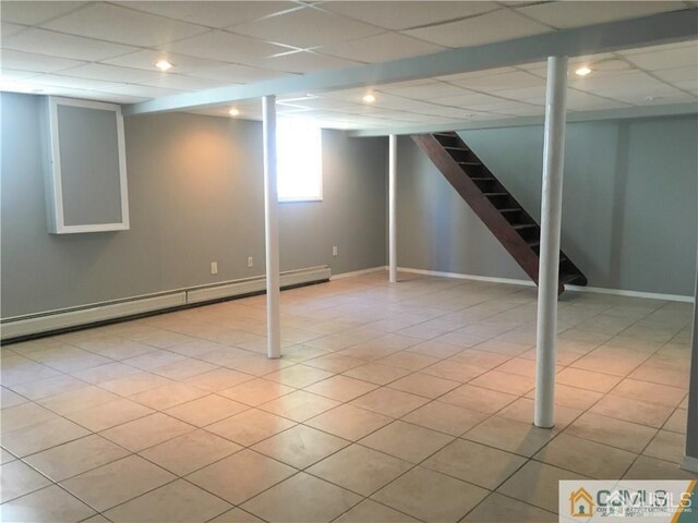 basement with baseboards, a drop ceiling, a baseboard radiator, stairway, and tile patterned floors