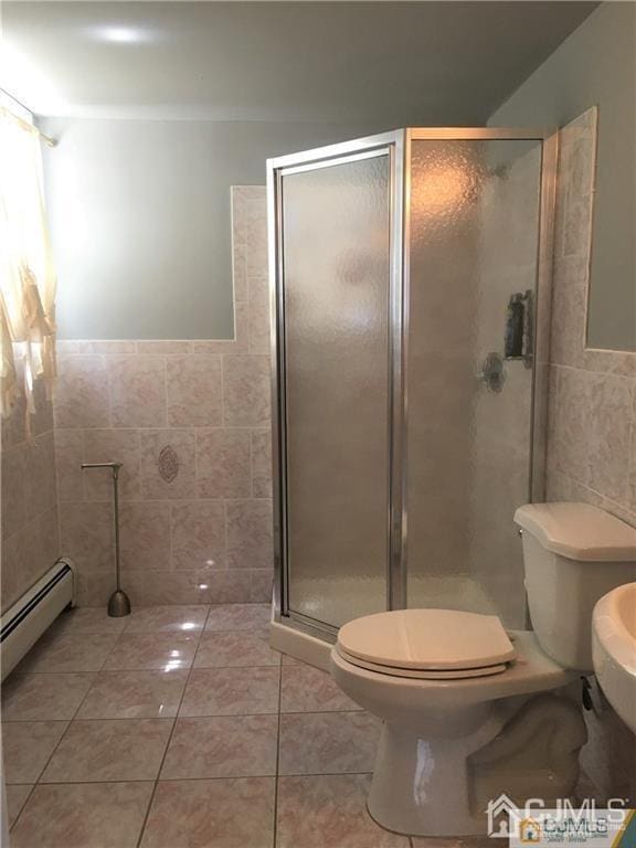 bathroom featuring toilet, a stall shower, tile patterned flooring, and tile walls