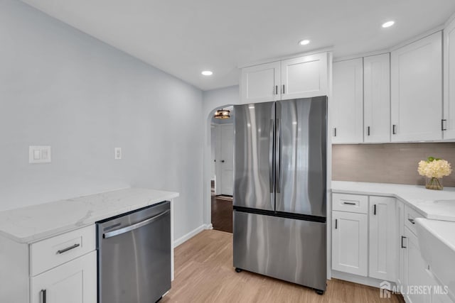 kitchen with arched walkways, tasteful backsplash, light wood-style flooring, appliances with stainless steel finishes, and light stone countertops