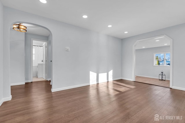 spare room featuring baseboards, arched walkways, wood finished floors, and recessed lighting