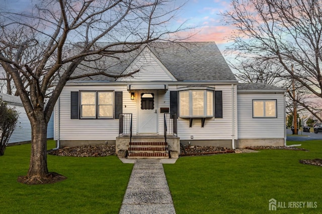 bungalow featuring a yard and roof with shingles