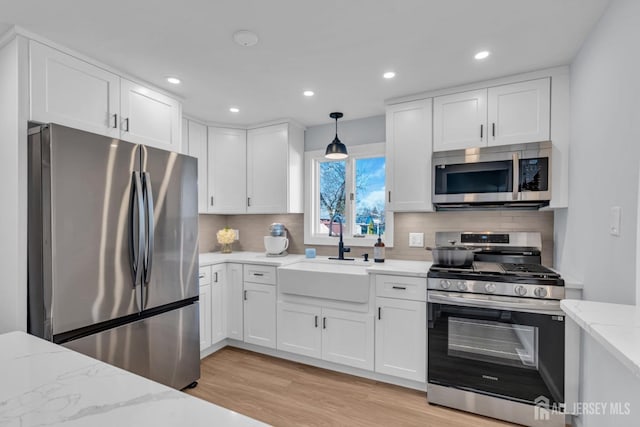 kitchen with white cabinets, decorative backsplash, light stone countertops, stainless steel appliances, and a sink