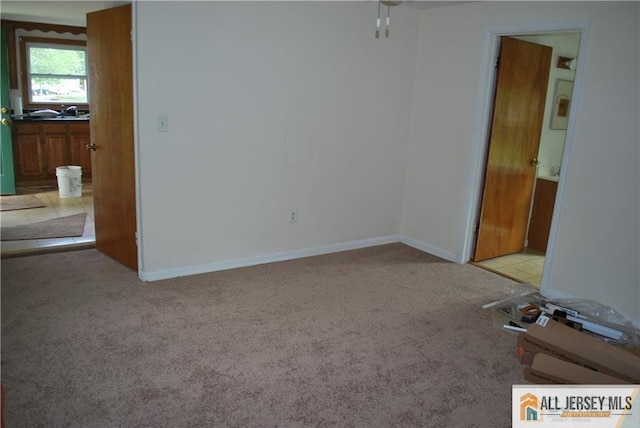 empty room with a sink, baseboards, and light carpet