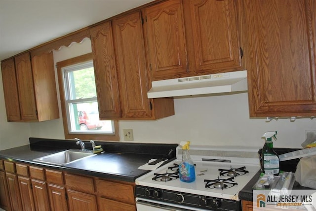 kitchen featuring brown cabinetry, white gas range oven, a sink, and under cabinet range hood