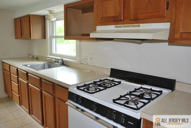 kitchen with under cabinet range hood, brown cabinetry, a sink, and white gas range